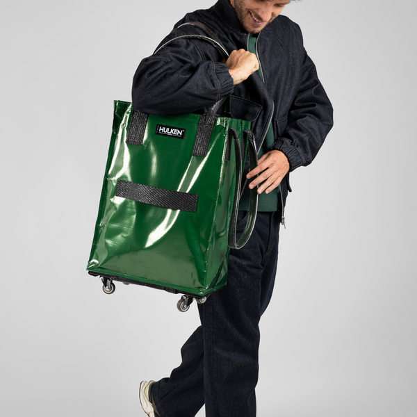 Person holding a forest green rolling bag with 'HUKEN' branding on a gray background